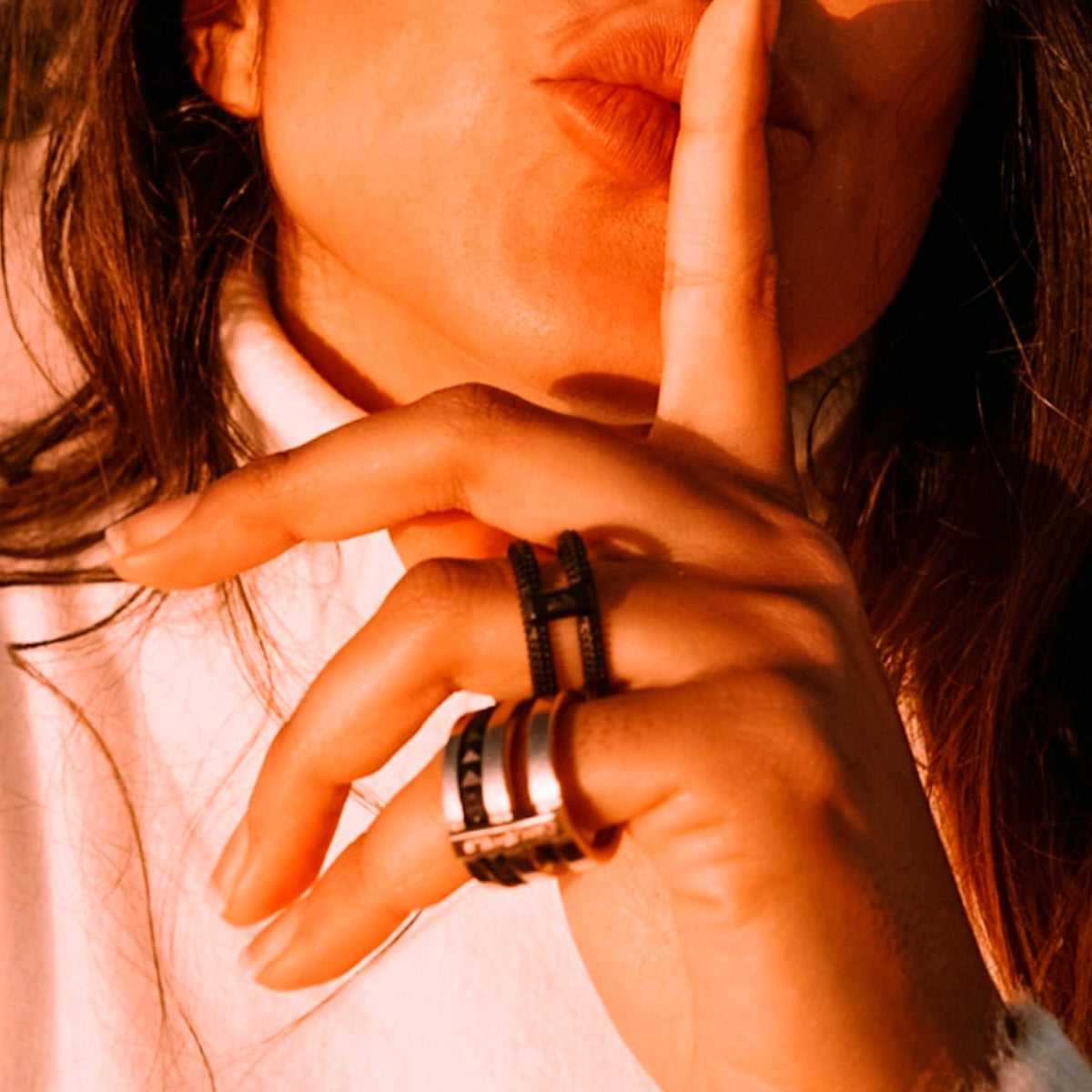 Woman wearing rings from AN JEWELS JEWELRY Mod. AR.R2NS02BK-7, finger on lips suggesting silence, in bright sunlight.